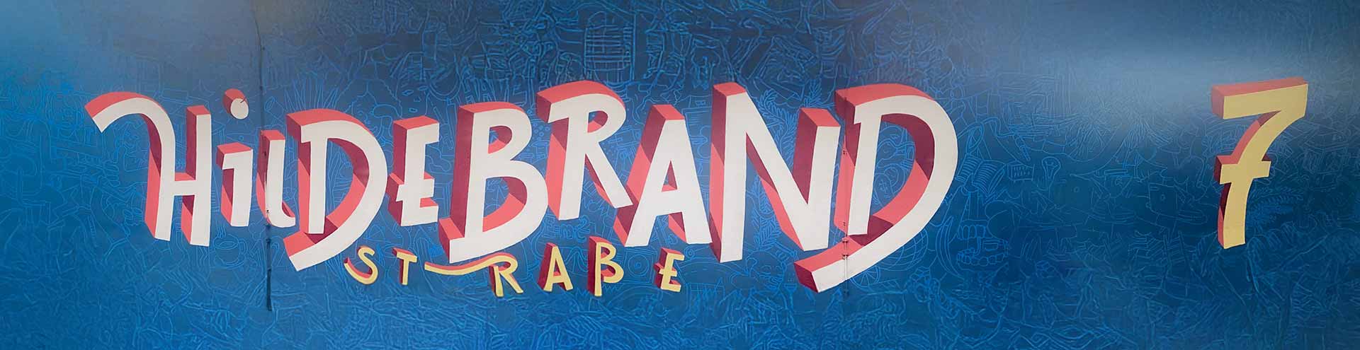 Graffiti-Schriftzug „Hildebrandstrasse“ mit gelber Nummer 7 auf blauem Hintergrund am Studentenwohnheim Hildebrandstrasse Dresden