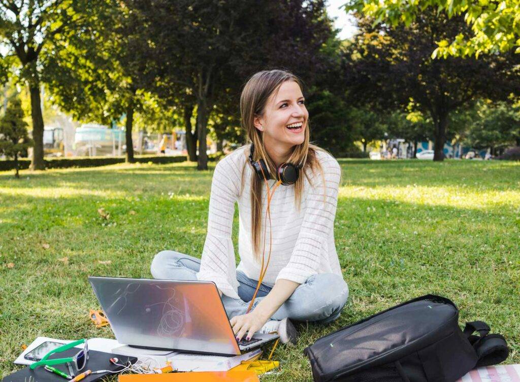 Studentin sitzt im Park mit Laptop und Kopfhoerern, entspanntes Lernen nahe dem Studentenwohnheim Hildebrandstrasse Dresden