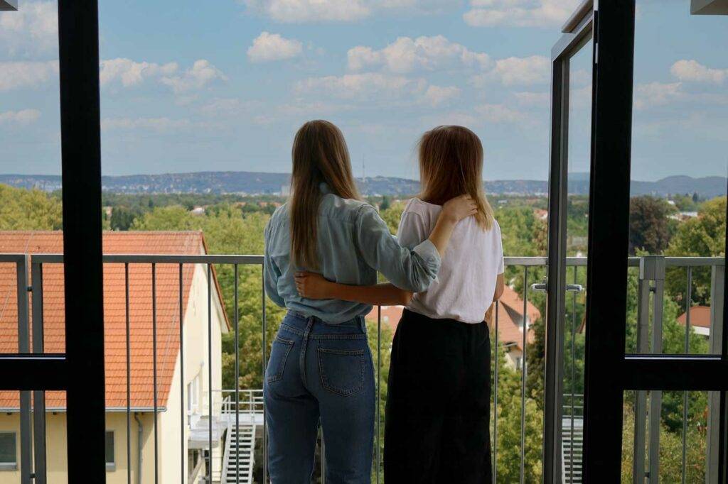 Zwei Studentinnen auf dem Balkon des Studentenwohnheims Hildebrandstraße Dresden blicken auf die Stadt
